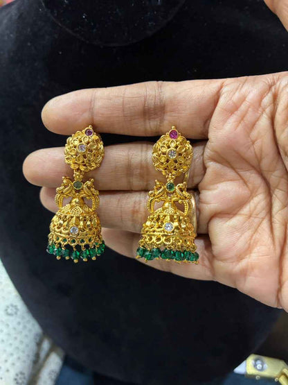 Gold-plated temple-style jhumka earrings feature a Lakshmi or peacock motif